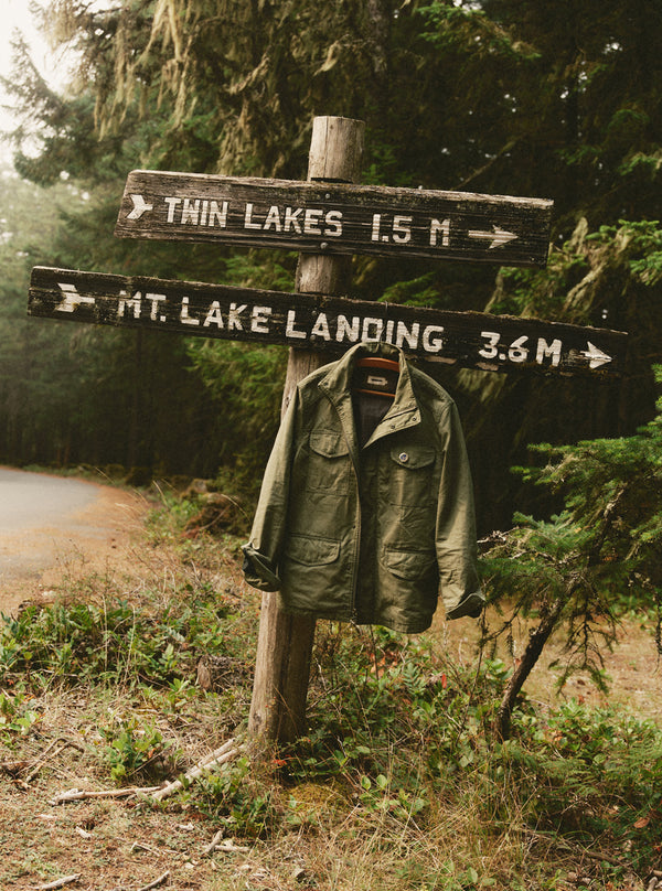 The Field Jacket in Burnt Olive Ripstop by a sign post
