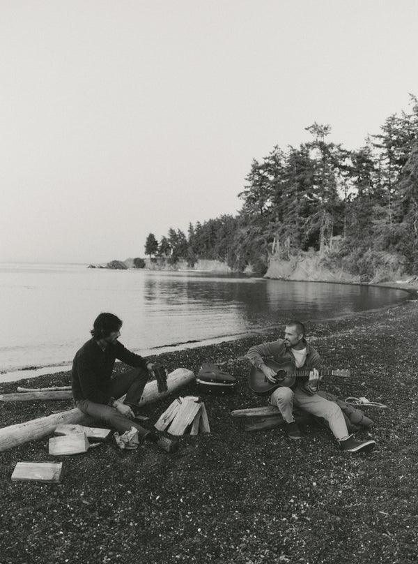 Two guys sitting by the shore, playing a guitar
