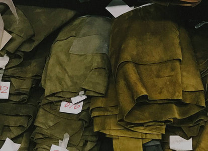 Stacks of olive green fabrics are arranged and labeled with white notecards bearing handwritten red numbers.