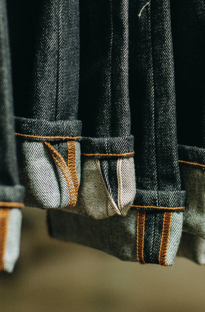 A closeup image of five cuffed denim pant legs suspended from out of frame.