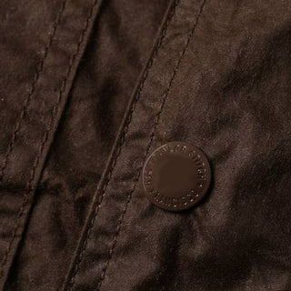 Closeup image of a brown waxed cotton canvas with stitched seams and a tonal metal button.