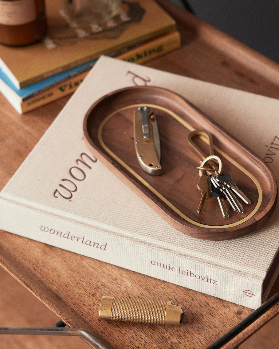 The Valet Tray in Walnut and Brass on a book, Accessories by Taylor Stitch