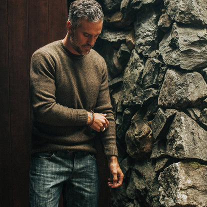 Our guy cinching up the sleeve on his sweater, standing next to a rough-hewn stone wall.