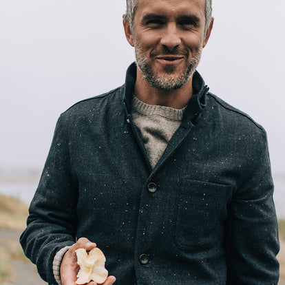 Our guy eating an apple, with his shirt bottuned up, collar popped, over a sweater.