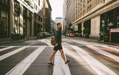 A guy in shorts and fleece walking over a zebra crossing.