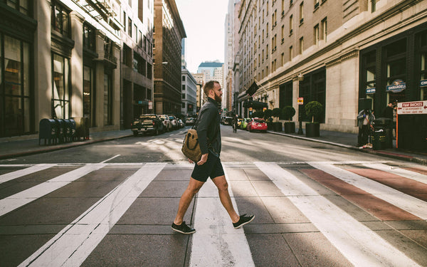 A guy in shorts and fleece walking over a zebra crossing.