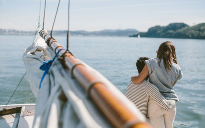 A couple sitting on the bow of a boat, shot from the mast, looking along the boom.