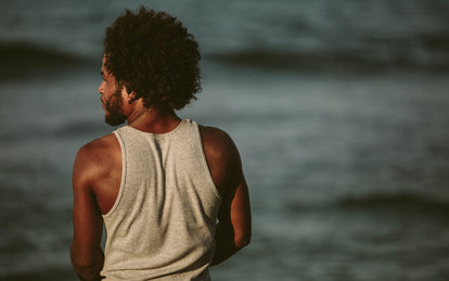 A guy wearing a vest, standing on the sea shore, with the ocean in the background.