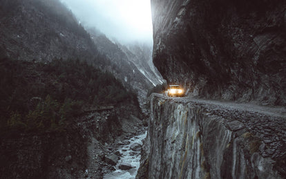 A 4x4 traversing an impossibly-engineered cliffside track through rugged mountains.