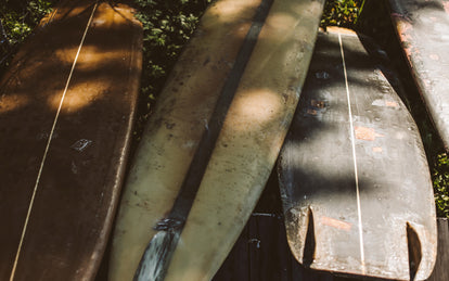 Four well-used surfboards laying out on grass.