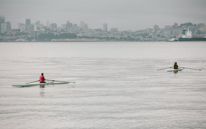 Two people rowing through the bay with SF in the background.