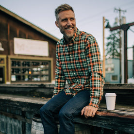 Fit model smiling while sitting on a ledge with a cup of coffee wearing The Jack in Rust Plaid Oxford
