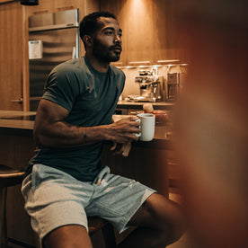 fit model sitting by the kitchen counter wearing The Merino Tee in Dark Slate