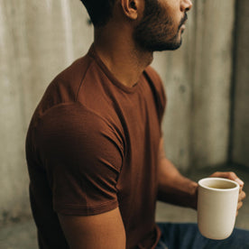 fit model holding a coffee cup and sitting in The Merino Tee in Russet