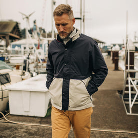 Fit model walking along the pier wearing The Navigator Jacket in Natural and Navy Colorblock