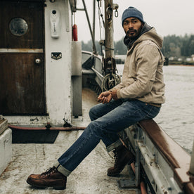 fit model sitting on the edge of a boat in The Workhorse Hoodie in Sand Boss Duck