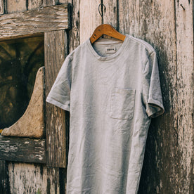 material shot outdoors of The Botanical Dye Tee in Grey, hanging on shed