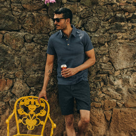 fit model wearing The Camp Short in Navy Herringbone, holding beer, next to yellow chair