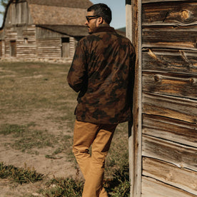 fit model leaning up against barn in The Field Jacket in Camo