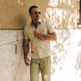 fit model wearing The Short Sleeve Officer Shirt in Khaki, leaning against wall