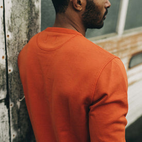 fit model leaning against a wall in The Fillmore Crewneck in Rust