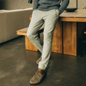 fit model leaning against a wooden table in The Fillmore Pant in Heather Grey