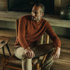 fit model sitting in a chair wearing The Lodge Sweater in Rust