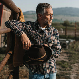 fit model wearing The Ledge Shirt in York Plaid, holding hat looking right