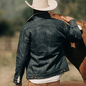 fit model wearing The Lined Long Haul Jacket in Green Cast Denim showing back while petting horse
