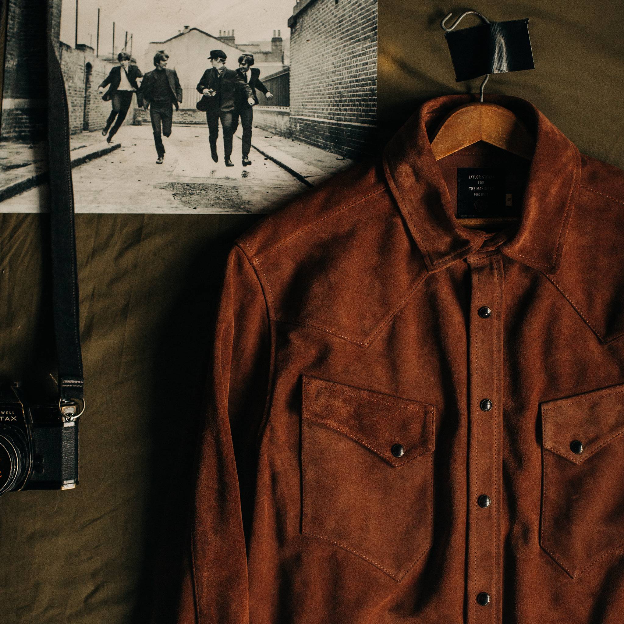 material shot of The Western Shirt in Espresso Suede hanging next to a photograph, Outerwear by Taylor Stitch