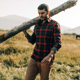 fit model carrying a log while wearing The Utility Shirt in Brushed Red Plaid