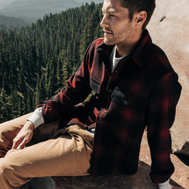 fit model sitting on a rock wearing The Explorer Shirt in Cardinal Plaid