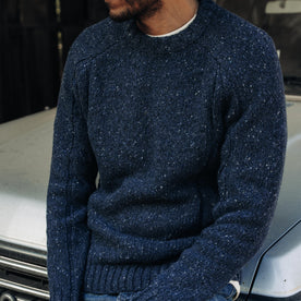 fit model sitting on a car wearing The Topside Sweater in Navy Donegal