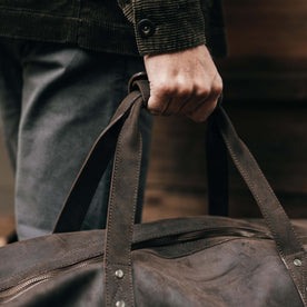 fit model holding the leather handles of The Weekender Duffle Bag in Espresso