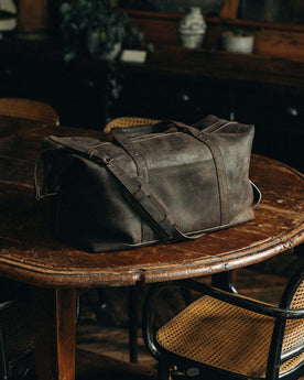 material shot of The Weekender Duffle Bag in Espresso on a wooden table, Accessories by Taylor Stitch