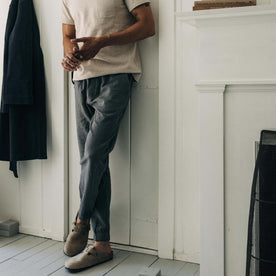 fit model leaning against the wall wearing The Apres Pant in Heather Grey Double Cloth
