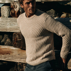 fit model wearing The Adirondack Sweater in Natural, leaning against fence
