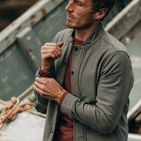 fit model wearing The Bomber Jacket in Charcoal Jungle Cloth, playing with sleeve near boat