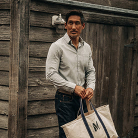 fit model wearing The California in Midnight Slub Micro Stripe, holding bag near wood wall