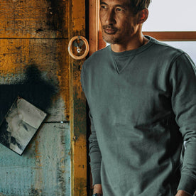 fit model wearing The Crewneck in Sea Green Terry, in boathouse, leaning against window