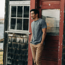 fit model wearing The Heavy Bag Tee in Charcoal, standing next to red door