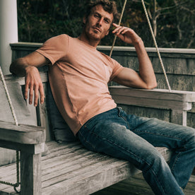 fit model wearing The Heavy Bag Tee in Dusty Rose, sitting on bench, looking at camera