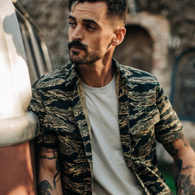 fit model wearing The Jungle Shirt in Tiger Camo, leaning against van, cropped shot