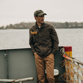 fit model wearing The Longshore Jacket in Dark Oak Waxed Canvas, near water, looking right