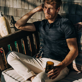 fit model wearing The Polo in Dark Navy Jacquard, sitting, holding glass of water