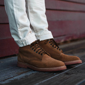 fit model wearing The Trench Boot in Butterscotch Weatherproof Suede, next to red wall, Footwear by Taylor Stitch
