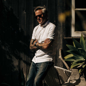 our fit model wearing The Short Sleeve Jack in Washed White Oxford outside on a fence with his arms crossed