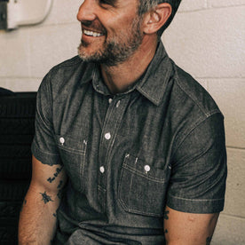 our fit model wearing The Short Sleeve Popover in Charcoal Chambray—sitting in the garage, cropped shot smiling 