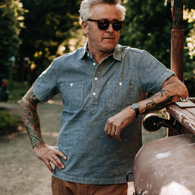 our fit model wearing The Short Sleeve Popover in Blue Chambray—looking left, shoulder on truck