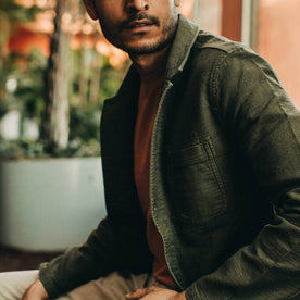 fit model wearing The Emerson Jacket in Olive Double Cloth, looking right of camera sitting down